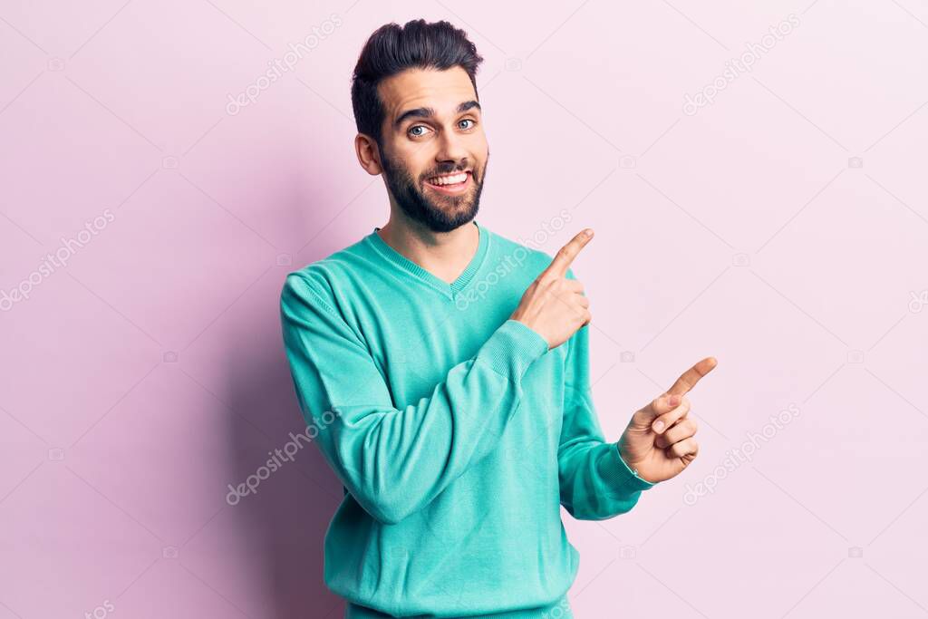 Young handsome man with beard wearing casual sweater smiling and looking at the camera pointing with two hands and fingers to the side. 