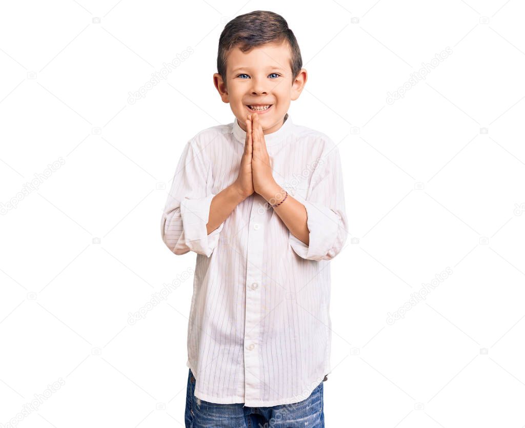 Cute blond kid wearing elegant shirt praying with hands together asking for forgiveness smiling confident. 