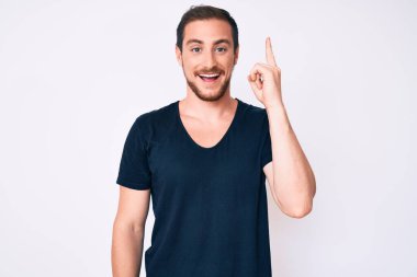 Gündelik giysiler giymiş genç yakışıklı bir adam başarılı bir fikri işaret ediyor. Heyecanlı ve mutlu. Bir numara.. 