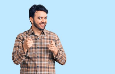 Günlük kıyafetler giyen genç İspanyol adam mutlu ve komik yüzüyle kamerayı işaret ediyor. iyi enerji ve titreşimler. 