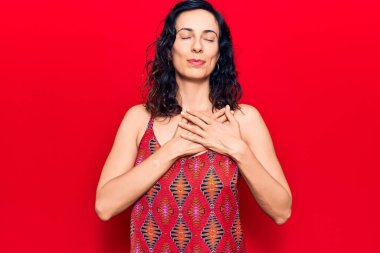 Gündelik kıyafetler giyen, göğsünde elleri, yüzünde minnet dolu bir jestle gülümseyen genç ve güzel bir İspanyol kadın. sağlık kavramı. 