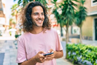 Genç İspanyol adam şehirde akıllı telefon kullanarak mutlu gülümsüyor..