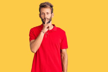 Sakallı, sıradan kıyafetler giyen, dudakları parmaklarıyla sessiz olmak isteyen yakışıklı sarışın adam. sessizlik ve gizli konsept. 