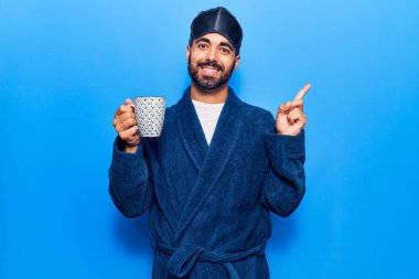 Uyku maskesi takan ve sabahlık giyen genç İspanyol adam kahvemi yudumlarken gülümsüyor. 