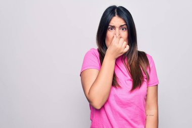 Genç, güzel, esmer, sıradan pembe tişörtler giyen, beyaz arka planda duran, pis ve iğrenç bir koku alan, nefesini burnunda tutan bir kadın. Kötü kokuyor.