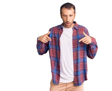 Gündelik kıyafetler giyen genç yakışıklı adam parmaklarını göstererek reklamını yapıyor, şaşırmış yüz ve ağzını açıyor. 