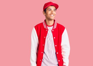 Beyzbol üniforması giyen genç Afro-Amerikan bir adam yüzünde gülümseme, doğal bir ifade ile yan yana bakıyor. Kendinden emin gülen. 