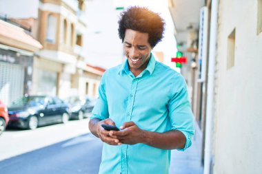 Genç, yakışıklı, Afro-Amerikan bir adam günlük giysiler giyip mutlu gülümsüyor. Yüzünde gülümsemeyle şehrin caddesinde akıllı telefon kullanarak dikiliyorsun..