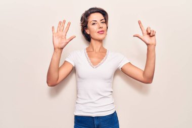 Genç ve güzel bir kadın gündelik giysiler giyer ve yedi numaralı parmaklarıyla işaret ederken kendinden emin ve mutlu bir şekilde gülümser.. 