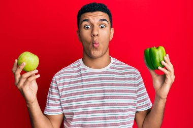 Genç Arap adam elinde yeşil elma ve biber tutarak balık suratlı ve şaşı gözlü, çılgın ve komik.. 