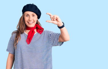 Fransız beresi takan, çizgili tişört giyen, gülümseyen, kendine güvenen, el hareketi yapan, parmaklarıyla işaret yapan güzel sarışın bir kadın ve kamera. ölçüm kavramı. 