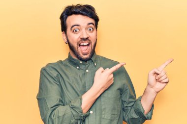 Gündelik kıyafetler giyen genç İspanyol adam gülümseyip kameraya bakıyor ve iki eliyle ve parmaklarıyla kenarı işaret ediyor.. 