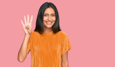 Genç esmer Arap kadın, günlük kıyafetler giyiyor ve dört numarayı gösterip işaret ederken kendinden emin ve mutlu gülümsüyor.. 