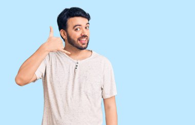 Günlük kıyafetler giymiş, gülümseyen genç İspanyol adam telefonla el ve parmak hareketleri yapıyor telefonda konuşur gibi. iletişim kavramları. 