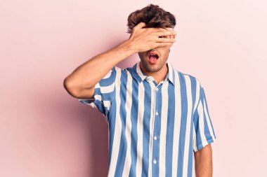 Gündelik kıyafetler giyen genç İspanyol adam şok içinde yüzünü ve gözlerini eliyle kapatıyor, parmaklarından korkuyla bakıyor. 