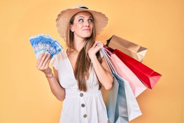 Genç sarışın kız alışveriş torbaları ve Güney Afrikalı paralar tutuyor. Gülümsüyor ve başka tarafa bakıyor.. 