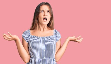 Güzel, beyaz bir kadın, günlük kıyafetler giymiş, deli deli deli bağırıyor, agresif bir ifadeyle bağırıyor ve kollarını kaldırıyor. hüsran kavramı. 