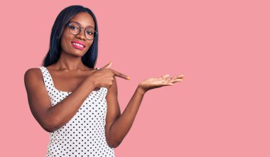 Genç Afrikalı Amerikalı kadın gündelik kıyafetler ve gözlük takıyor kameraya hayret ediyor ve gülümsüyor.. 