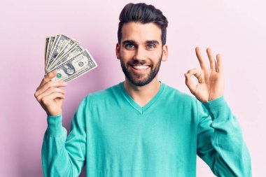 Sakallı, elinde bir tomar para olan yakışıklı genç adam parmaklarıyla imza atıyor, gülümsüyor ve mükemmel bir sembol. 