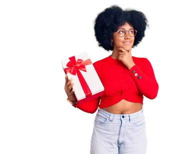 Genç Afrikalı Amerikalı kız, eli çenesinde hediyesini tutarken soru sormayı, düşünceli ifadeyi düşünüyor. Gülümseyen ve düşünceli bir yüz. şüphe kavramı. 