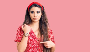 Yazlık elbise giyen esmer kız saati, sabırsızlığı ve rahat bir ifadeyle kameraya bakmayı işaret ediyor. 