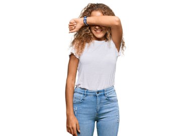 Beyaz günlük beyaz tişörtler giyen güzel beyaz kız kollarıyla gözlerini kapayarak neşeli ve komik gülümsüyor. kör kavram. 