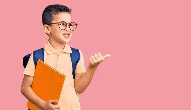 Okul çantası takmış, elinde kitapla baş parmağını kaldırıp gülümseyen, ağzı açık bir çocuk. 