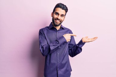 Sakallı, sıradan tişörtlü, genç ve yakışıklı bir adam kameraya hayret ediyor ve gülümsüyor.. 