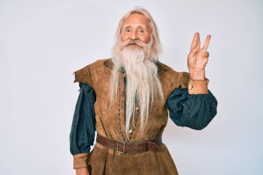 Gri saçlı, uzun sakallı, Viking kostümü giyen, üç numarayı işaret eden, kendinden emin ve mutlu gülümseyen yaşlı adam.. 