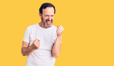 Sıradan tişörtler giyen orta yaşlı yakışıklı adam kolları havada ve gözleri kapalı bir şekilde başarıyı kutluyor ve şaşırıyor. Kazanan konsept. 