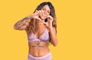 Dövmeli, iç çamaşırlı, aşık gülümseyen, elleriyle kalp sembolü yapan genç bir İspanyol kadın. romantik kavram. 