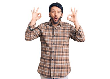 Gündelik kıyafetler giyen genç İspanyol adam şaşırmış ve şok olmuş görünüyor. Tamam sembolünü parmaklarıyla yapıyor. çılgın ifade 