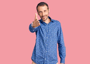 Gündelik kıyafetler giyen genç yakışıklı adam dostça bir selamlama ve hoş geldin hediyesi olarak el sıkışmayı sunuyor. başarılı iş. 