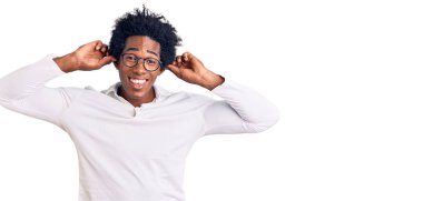 Afro saçlı, sıradan kıyafetler giyen ve gözlüklü parmaklarıyla kulaklarını çeken yakışıklı Afro-Amerikan bir adam. Komik bir jest. deneme sorunu 