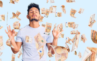 Yakışıklı Latin Amerikalı, günlük kıyafetler giyen rahat ve gözleri kapalı gülümseyen parmaklarıyla meditasyon hareketi yapan genç adam. yoga konsepti.