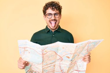 Kıvırcık saçlı, elinde şehir haritası olan genç, beyaz bir adam komik bir ifadeyle dilini dışarı çıkartıyor.. 