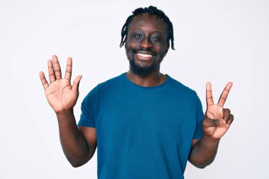 Saçları örgülü genç Afro-Amerikan bir adam 7 numaralı parmaklarını gösterip gösterirken kendinden emin ve mutlu bir şekilde gülümsüyor.. 