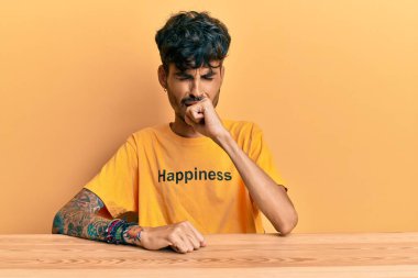 Üzerinde mutluluk mesajı olan İspanyol tişörtü giyen genç adam kendini iyi hissetmiyor ve soğuk algınlığı veya bronşitin belirtisi olarak öksürüyor. sağlık hizmeti kavramı. 