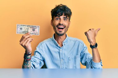 Masada oturan 50 dolarlık banknot tutan İspanyol genç adam başparmağıyla yan tarafa bakıyor ve ağzı açık gülümsüyor. 