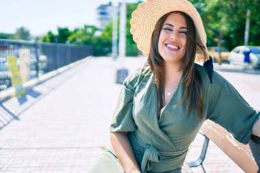 Genç İspanyol kadın tatilde gülümsüyor. Mutlu bir şekilde şehrin sokaklarında bankta oturuyor.