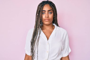 Saçları örgülü genç Afro-Amerikan kadın ciddi bir ifadeyle günlük yaz gömleği giyiyor. Basit ve doğal bir şekilde kameraya bakıyorsun.. 