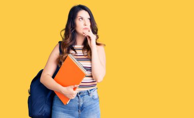 Güzel, genç, esmer bir kadın. Sırt çantası takıyor, kitap okuyor. Ciddi bir yüz ifadesi var. 