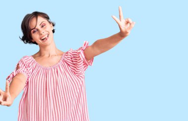 Kısa saçlı, sıradan yaz kıyafetleri giyen, dili dışarı fırlayan ve zafer işareti yapan genç ve güzel bir kadın. İki numara.. 