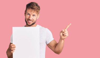 Boş pankart tutan beyaz bir genç. Gülümsüyor. Mutlulukla işaret ediyor. 