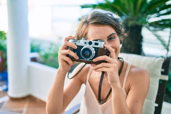 Genç, güzel, beyaz bir kadın, evinde mutlu bir şekilde gülümsüyor ve klasik kamera kullanarak fotoğraf çekiyor.