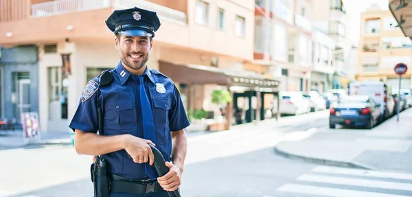 警察の制服を着た若いハンサムなパニック警官が笑顔で幸せ 町の通りに散弾銃を持って笑顔で立って — ストック写真