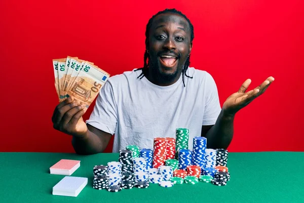 50 avroluk banknotlarla poker oynayan yakışıklı genç adam başarıyı mutlu bir gülümsemeyle kutluyor ve kazanan el kaldırarak ifade ediyor. 