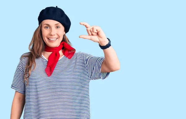 Fransız beresi takan, çizgili tişört giyen, gülümseyen, kendine güvenen, el hareketi yapan, parmaklarıyla işaret yapan güzel sarışın bir kadın ve kamera. ölçüm kavramı. 
