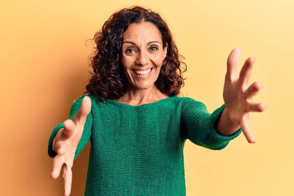 Orta yaşlı, güzel bir kadın sıradan bir kazak giyip kameraya bakıyor ve sarılmak için kollarını açmış gülümsüyor. Mutluluğu kucaklayan neşeli bir ifade.. 