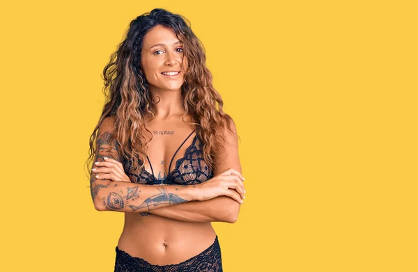 Young hispanic woman with tattoo wearing lingerie happy face smiling with crossed arms looking at the camera. positive person.